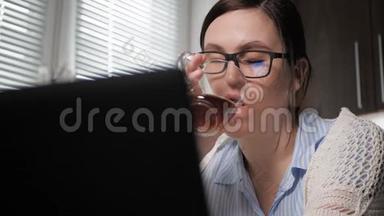 女孩喝绿茶或红茶。 厨房里貌美的女人的特写镜头看着笔记本电脑屏幕
